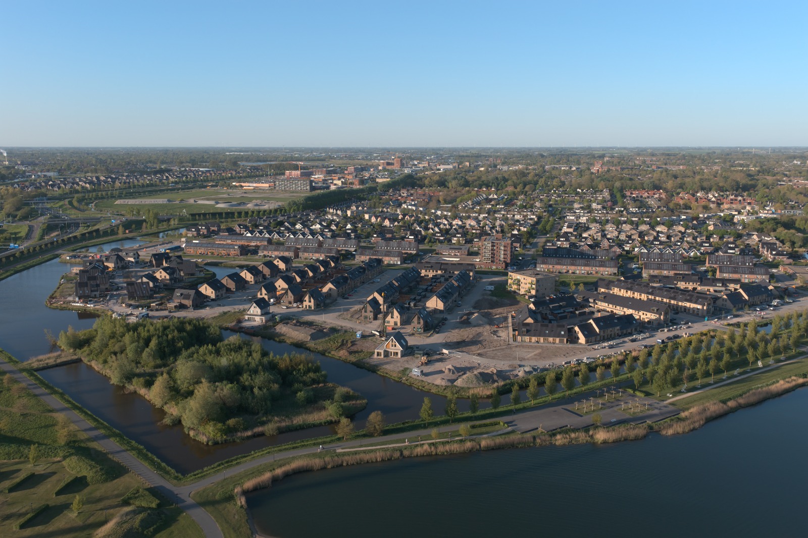 Luchtfoto van een nieuwbouwwijk aan het water, met de skyline van de stad op de achtergrond.